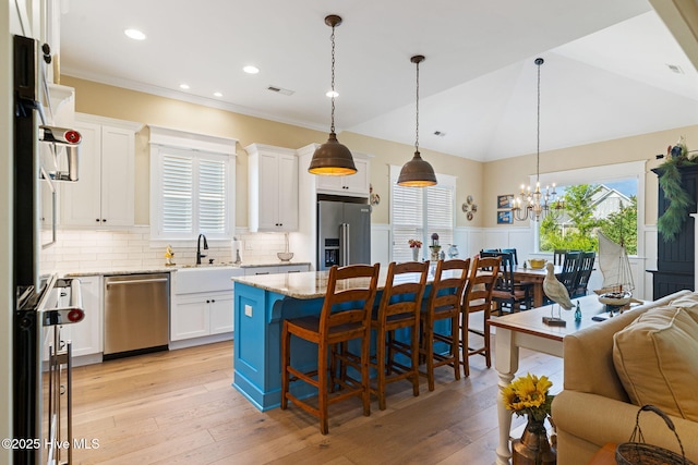kitchen with appliances with stainless steel finishes, a sink, wainscoting, a kitchen breakfast bar, and healthy amount of natural light