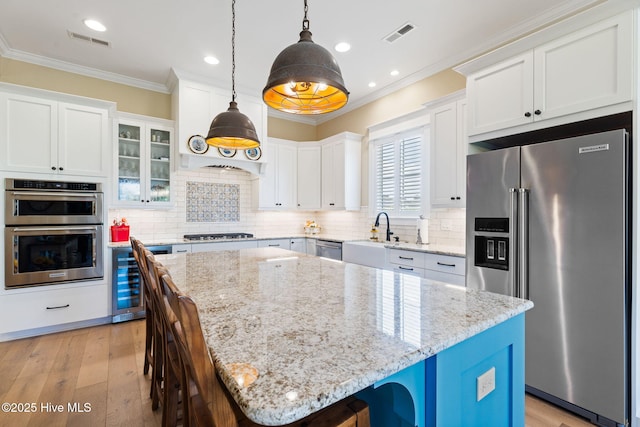 kitchen with appliances with stainless steel finishes, wine cooler, a sink, a kitchen bar, and crown molding