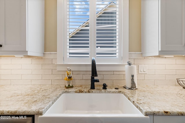 kitchen view of a sink, tasteful backsplash, light stone countertops, and white cabinetry