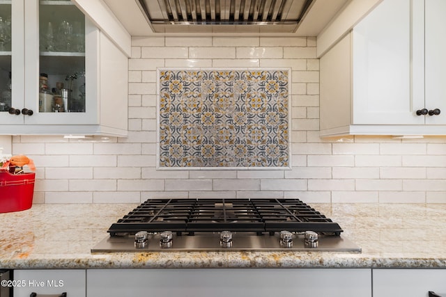 kitchen with stainless steel gas stovetop, white cabinetry, glass insert cabinets, backsplash, and light stone counters