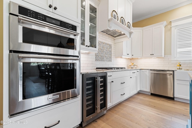 kitchen with wine cooler, stainless steel appliances, ornamental molding, white cabinets, and backsplash