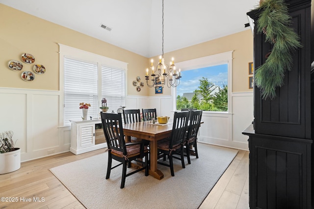 dining room with a decorative wall, a wainscoted wall, a chandelier, and light wood-style floors