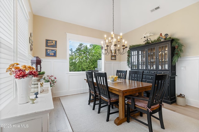 dining area with a chandelier, wainscoting, a decorative wall, and light wood-style flooring