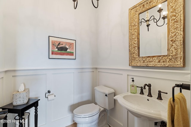 half bath with a decorative wall, a sink, wainscoting, and toilet
