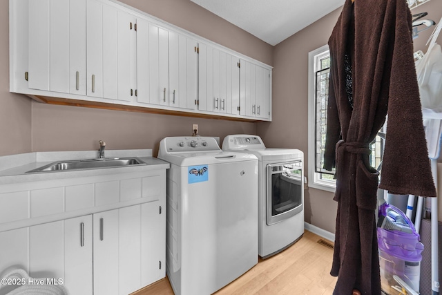 laundry room featuring washing machine and clothes dryer, cabinet space, plenty of natural light, and light wood finished floors