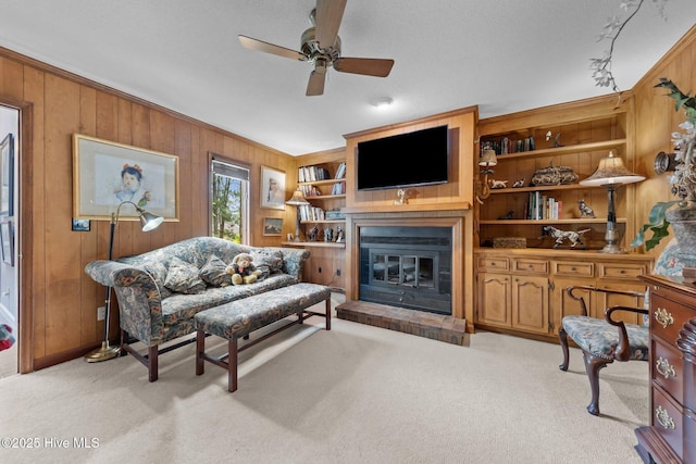 living room with wood walls, ceiling fan, light colored carpet, a glass covered fireplace, and ornamental molding