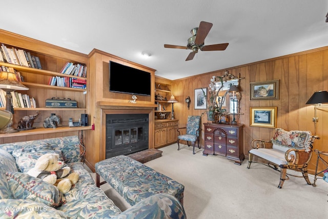 carpeted living area featuring a ceiling fan, wooden walls, a glass covered fireplace, and built in shelves