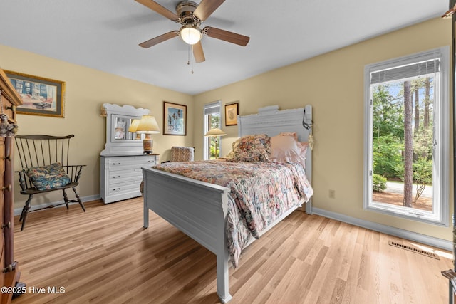 bedroom with multiple windows, light wood-style floors, and baseboards