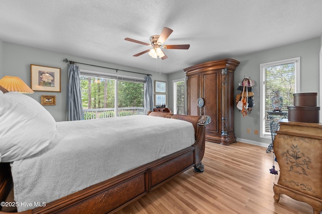 bedroom featuring baseboards, light wood finished floors, multiple windows, a ceiling fan, and a textured ceiling