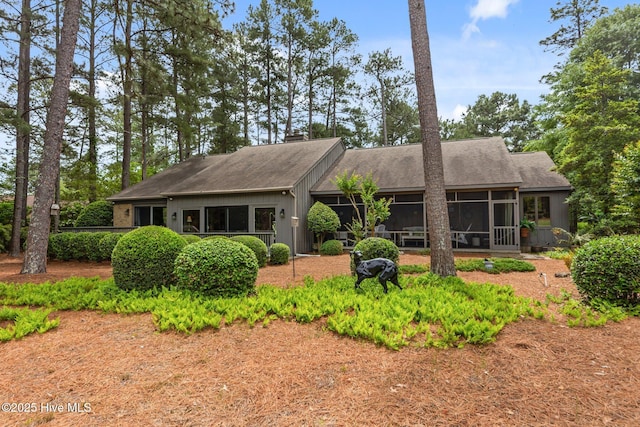 view of front of house with a sunroom, roof with shingles, and a chimney