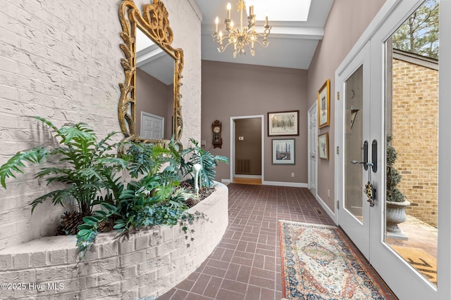 entrance foyer featuring a chandelier, brick patterned flooring, baseboards, and a high ceiling