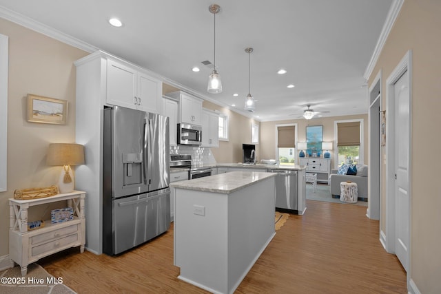 kitchen with ornamental molding, a kitchen island, stainless steel appliances, and ceiling fan