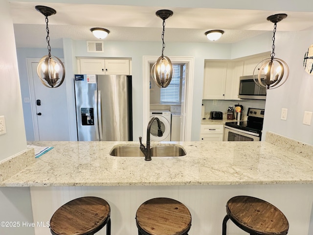 kitchen featuring light stone countertops, a sink, separate washer and dryer, visible vents, and appliances with stainless steel finishes