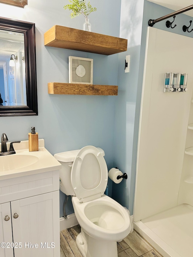 bathroom featuring toilet, a stall shower, wood finished floors, and vanity