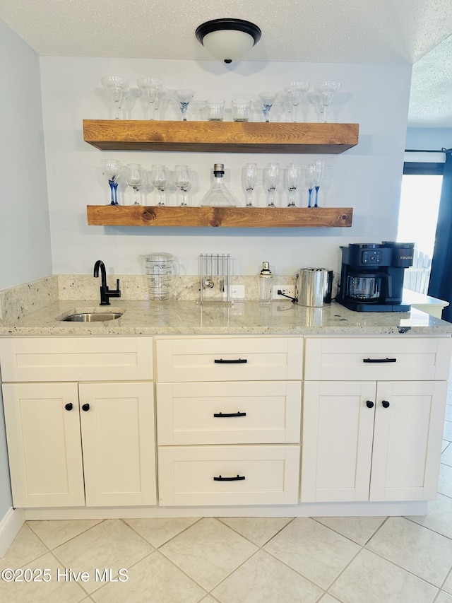 bar featuring light tile patterned floors, a textured ceiling, indoor wet bar, and a sink