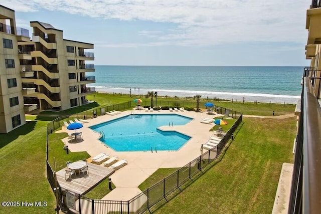 community pool with a yard, a water view, a patio area, and fence