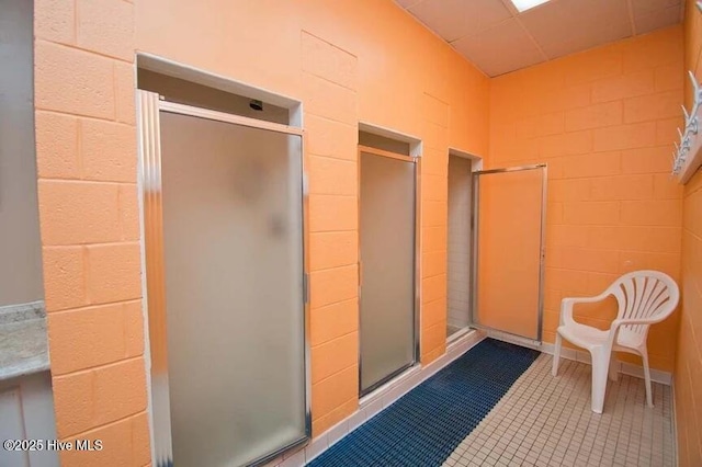 bathroom with concrete block wall, a stall shower, and tile patterned floors