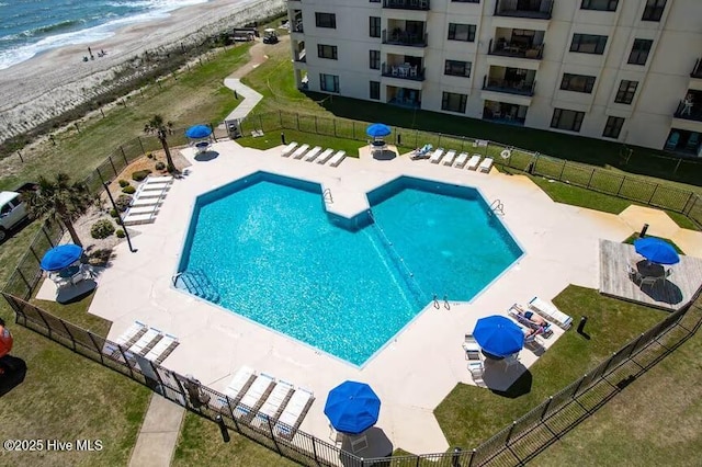 pool featuring fence, a patio area, a water view, and a view of the beach