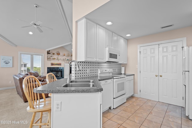 kitchen with white appliances, a sink, a ceiling fan, white cabinets, and a fireplace