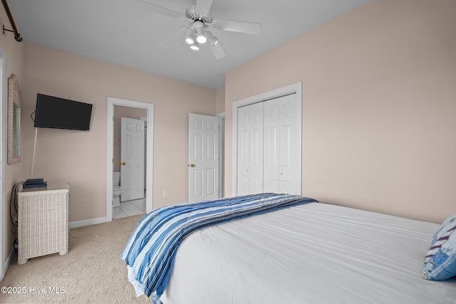 bedroom with light colored carpet, a closet, baseboards, ensuite bath, and ceiling fan