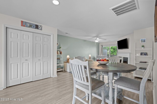 dining room featuring a ceiling fan, light wood finished floors, and a fireplace