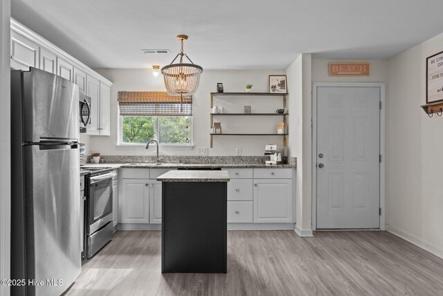 kitchen with appliances with stainless steel finishes, a sink, white cabinets, a kitchen island, and light wood-style flooring