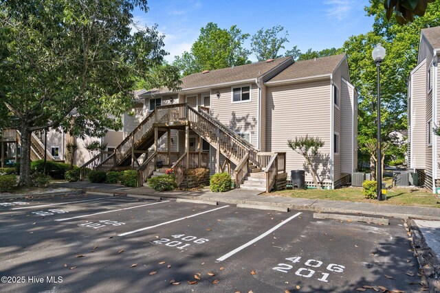 rear view of house with stairs, uncovered parking, and roof with shingles