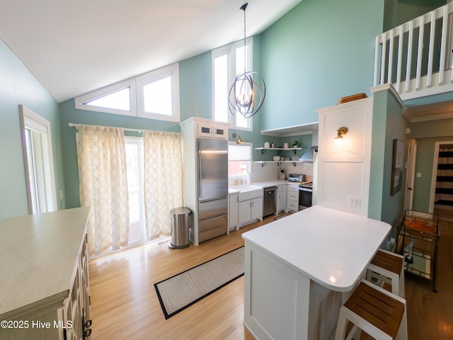 kitchen featuring appliances with stainless steel finishes, high vaulted ceiling, light countertops, a breakfast bar area, and open shelves