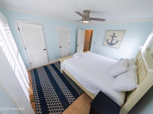 bedroom featuring ornamental molding, wood finished floors, two closets, and a ceiling fan