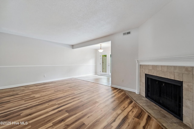 unfurnished living room with wood finished floors, a textured ceiling, visible vents, baseboards, and a tile fireplace