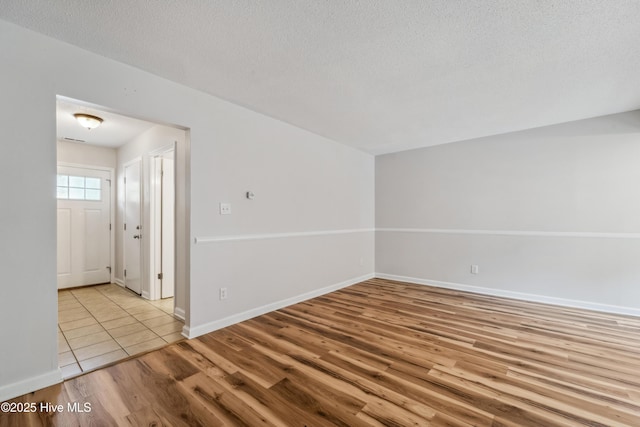 spare room with a textured ceiling, wood finished floors, and baseboards