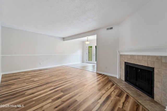 unfurnished living room with a textured ceiling, baseboards, visible vents, wood finished floors, and a tile fireplace