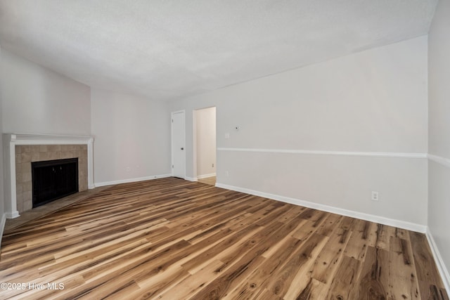 unfurnished living room with a tiled fireplace, wood finished floors, and baseboards