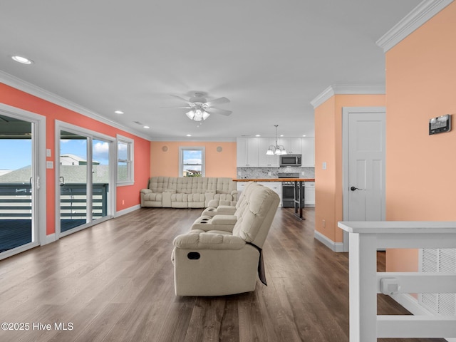 living area featuring dark wood-style flooring, recessed lighting, ornamental molding, and ceiling fan with notable chandelier