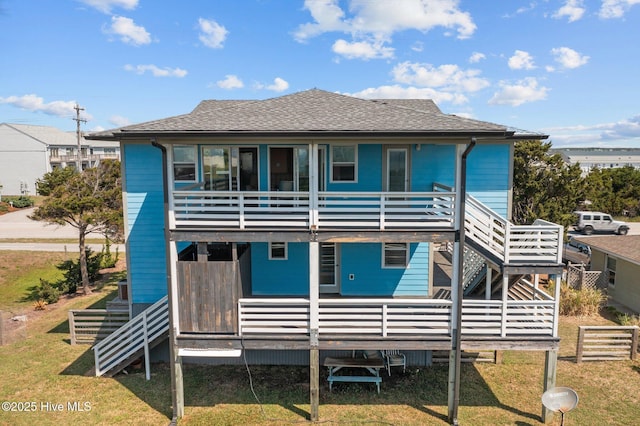 back of house featuring a deck, a shingled roof, stairs, and a lawn