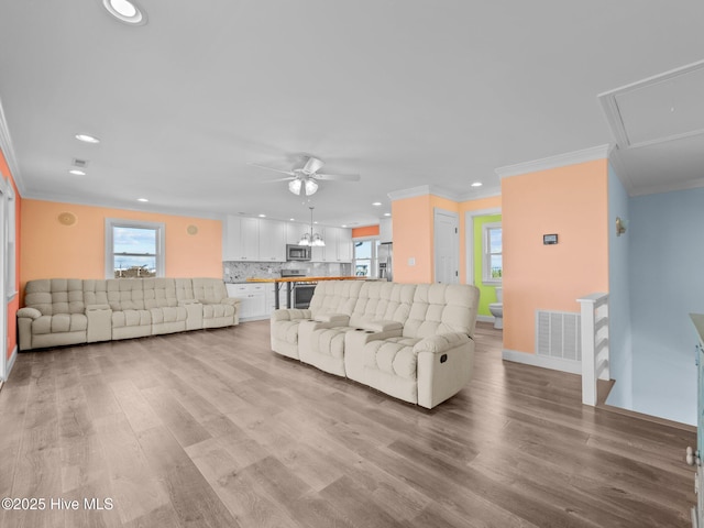 living area featuring visible vents, light wood-type flooring, recessed lighting, ornamental molding, and ceiling fan with notable chandelier