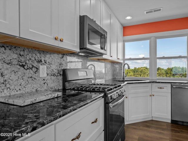 kitchen featuring a sink, dark wood-style flooring, stainless steel appliances, dark stone countertops, and white cabinetry