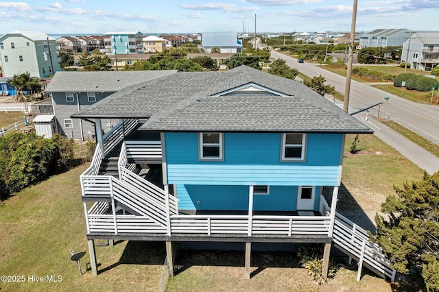 rear view of property with a residential view, a lawn, stairs, and a shingled roof
