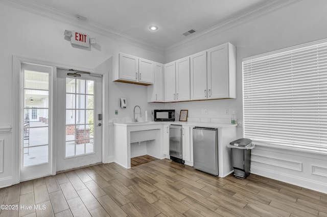 kitchen featuring black microwave, crown molding, light countertops, white cabinets, and light wood-style floors