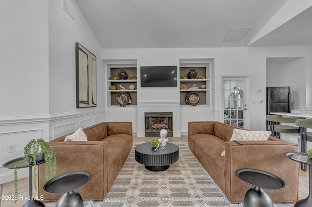 living area with visible vents, a decorative wall, built in features, vaulted ceiling, and a lit fireplace