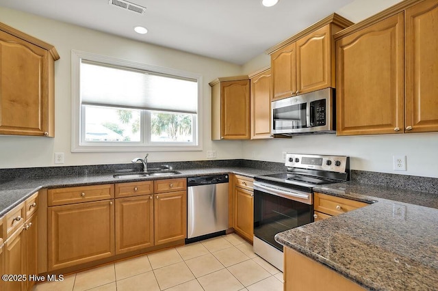1008 Garden Club Way, Leland, NC 28451 - kitchen featuring appliances with stainless steel finishes, a sink, light tile patterned floors, dark stone countertops, and brown cabinetry