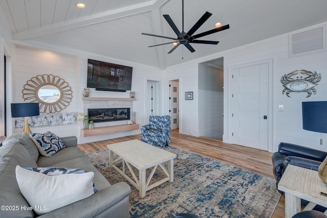 living room featuring lofted ceiling with beams, ceiling fan, wooden walls, and wood finished floors