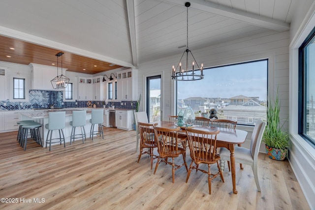 dining space featuring lofted ceiling with beams, a chandelier, and light wood-type flooring