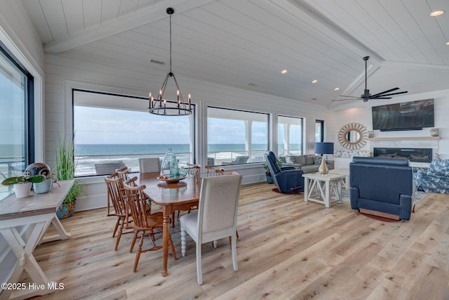 dining area featuring vaulted ceiling with beams, light wood-style floors, a water view, a glass covered fireplace, and visible vents