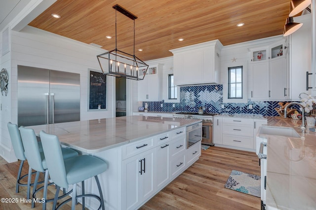 kitchen with light stone counters, wood ceiling, a kitchen island, a sink, and premium appliances