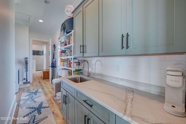 kitchen with light wood finished floors, light stone countertops, a sink, tasteful backsplash, and ornamental molding