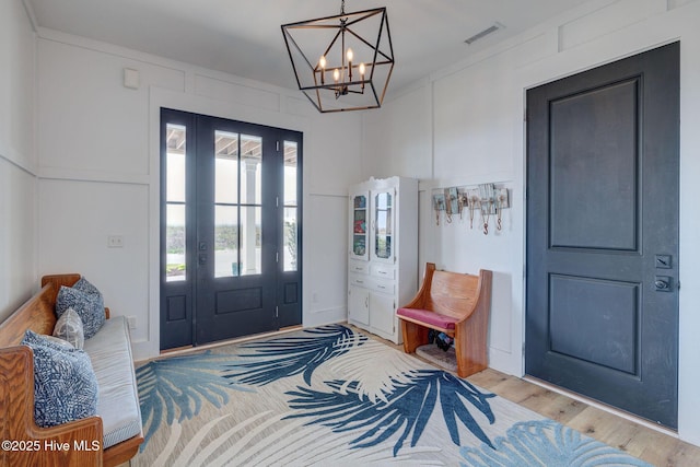 foyer entrance with light wood-style flooring, visible vents, and a notable chandelier
