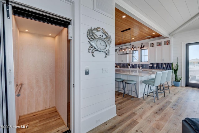 kitchen with elevator, wood ceiling, light countertops, white cabinets, and a kitchen breakfast bar