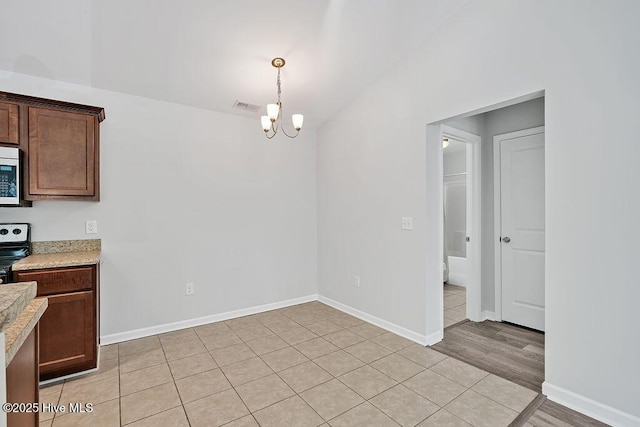 unfurnished dining area with an inviting chandelier, light wood-style floors, baseboards, vaulted ceiling, and visible vents