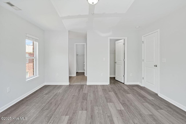 unfurnished bedroom with visible vents, a closet, wood finished floors, baseboards, and a spacious closet